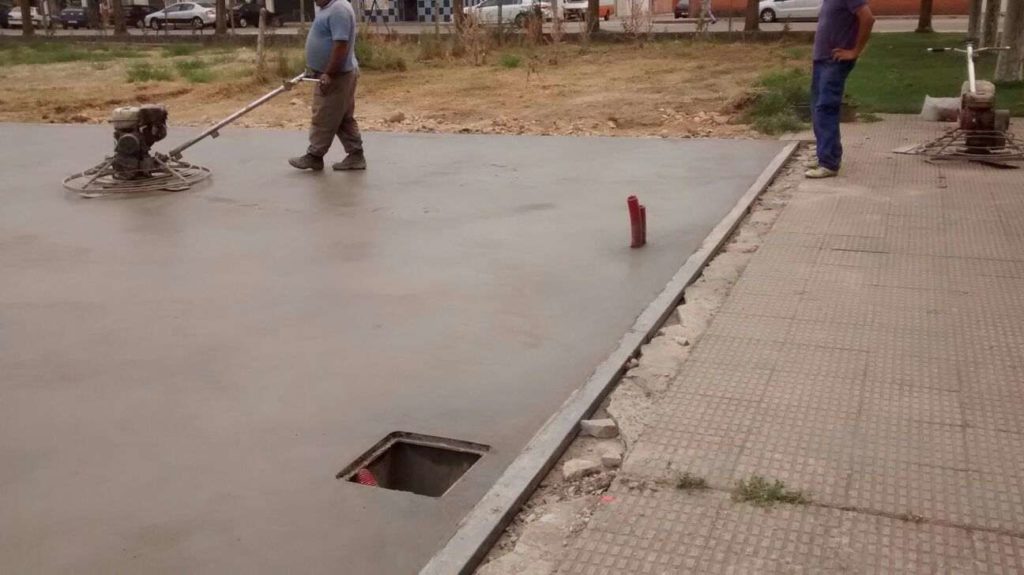 Two workers using machinery to finish a concrete surface in a construction area.