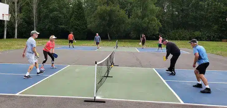 Mehrere Personen spielen Pickleball auf einem Platz mit Netzen und Markierungen.