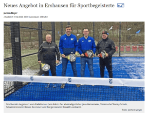 Four men standing on a padel court, each holding a padel racket and smiling at the camera.